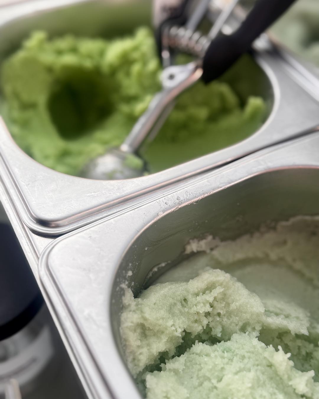 Two metal ice cream containers with sugar scrub and a scoop.